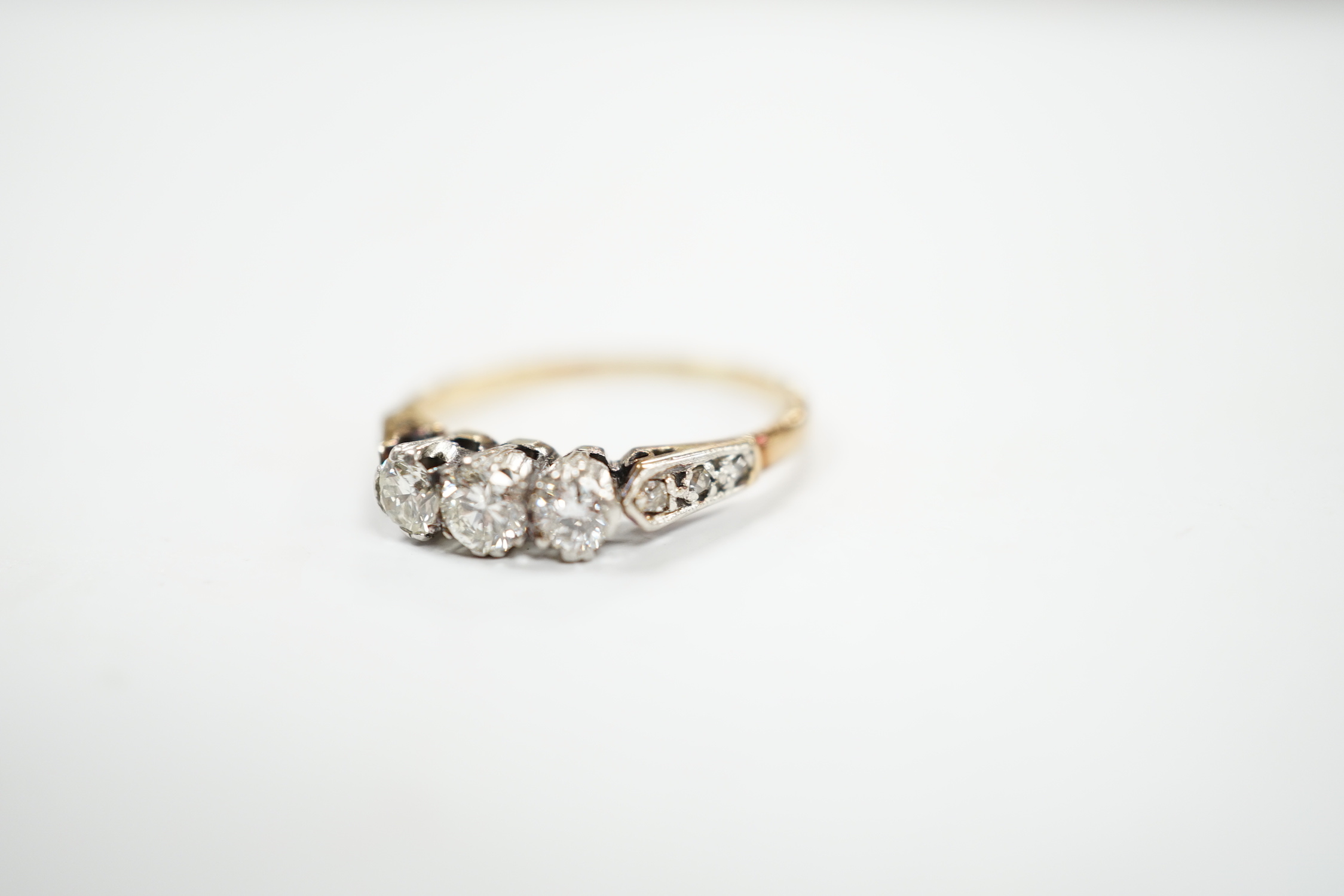 A yellow metal and three stone diamond set ring, with six stone diamond chip set shoulders, size L, gross weight 2.2 grams.